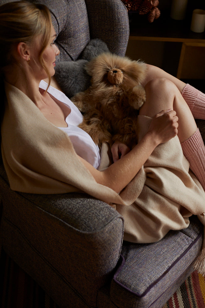 Woman sitting on a couch holding a small dog wrapped in a blanket